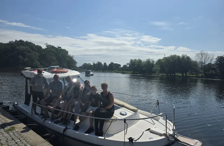 Goście Aquaczarter na dziobie houseboata Billy przy nabrzeżu na Pętli Żuławskiej w słoneczny dzień